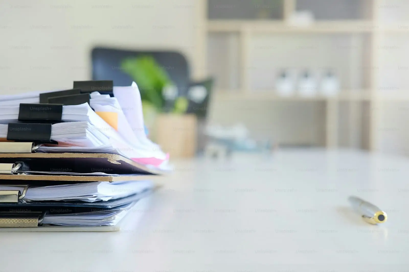 Stack of paper files and a pen on an office desk