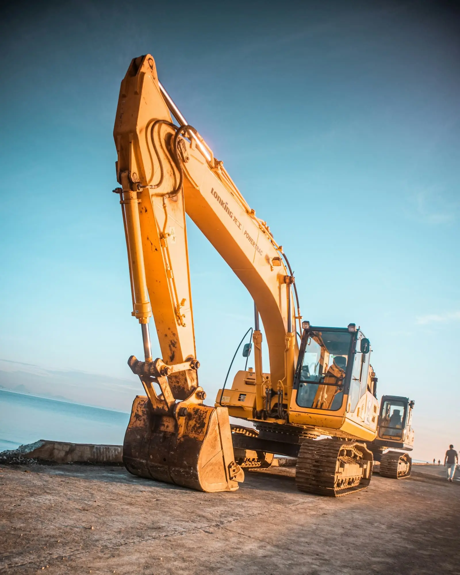 Yellow excavator working on grey rock beside a body of water in daylight