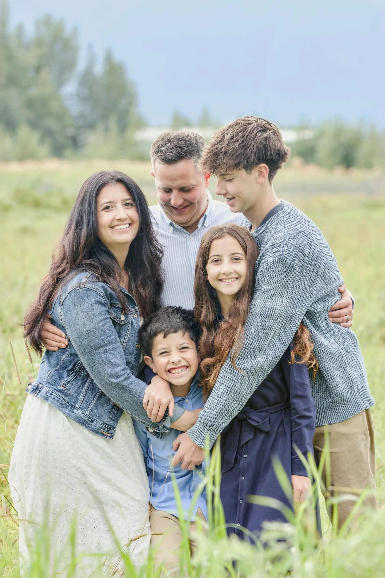 Happy family of five smiling together in a sunny grassy field
