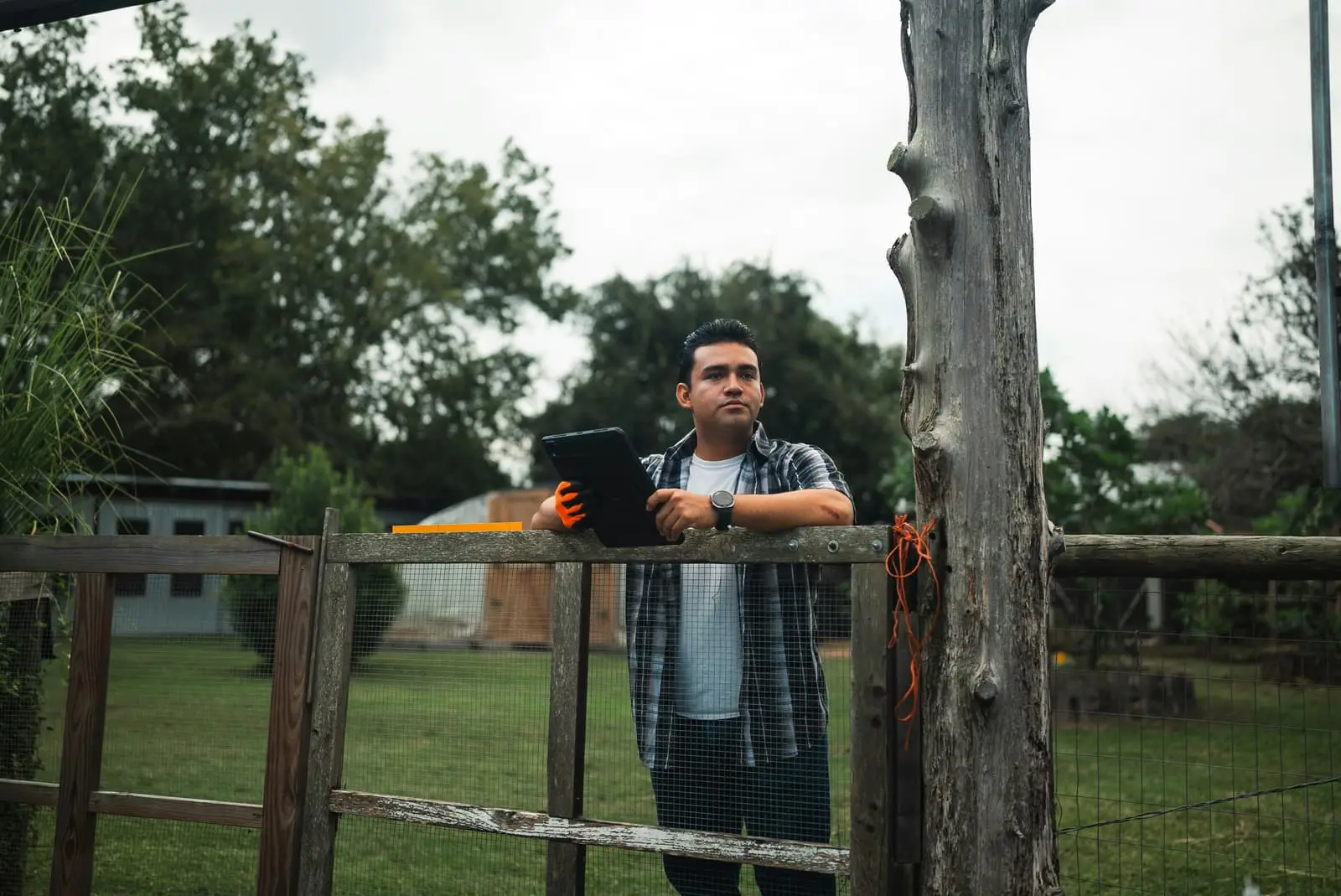 Man holding a tablet standing beside a wooden fence outdoors