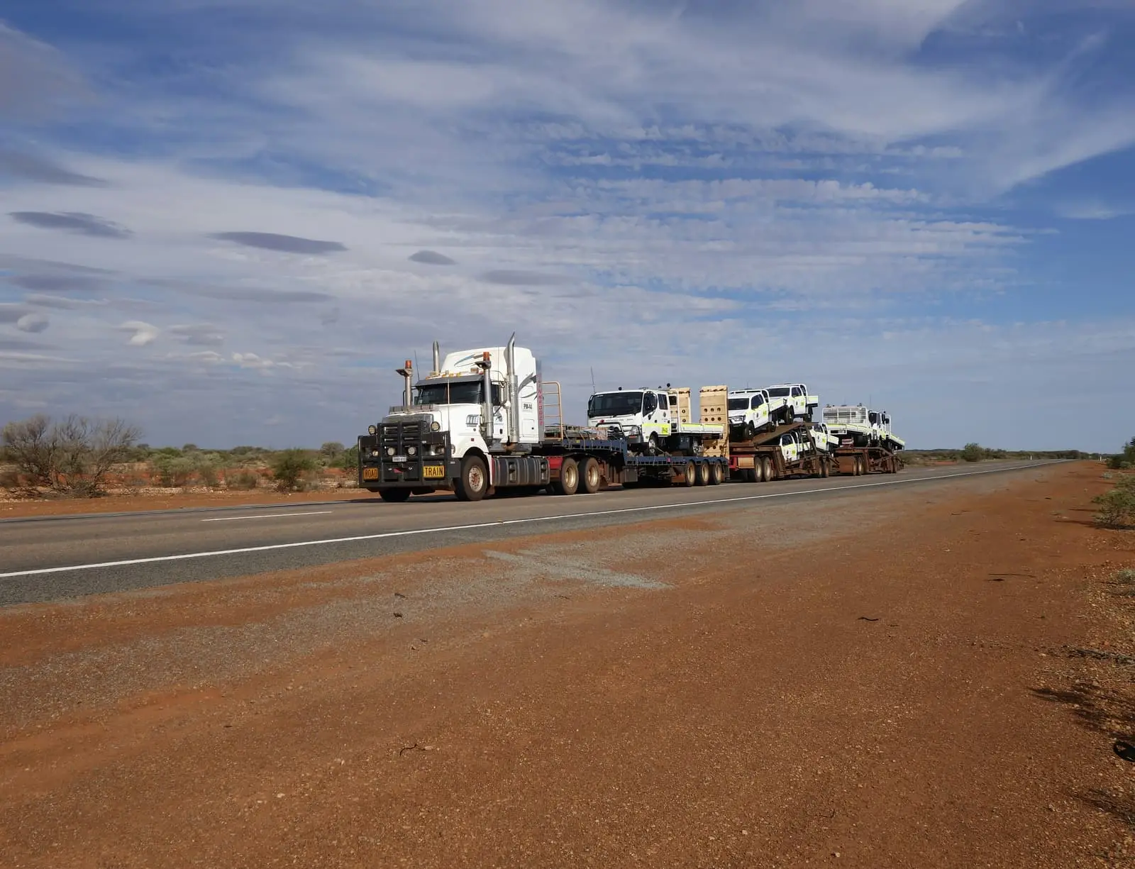 Road train hauling trucks along a red dirt road in the outback